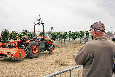 A visitor watches machinery operating among orchard trees at World Ag Expo 2026